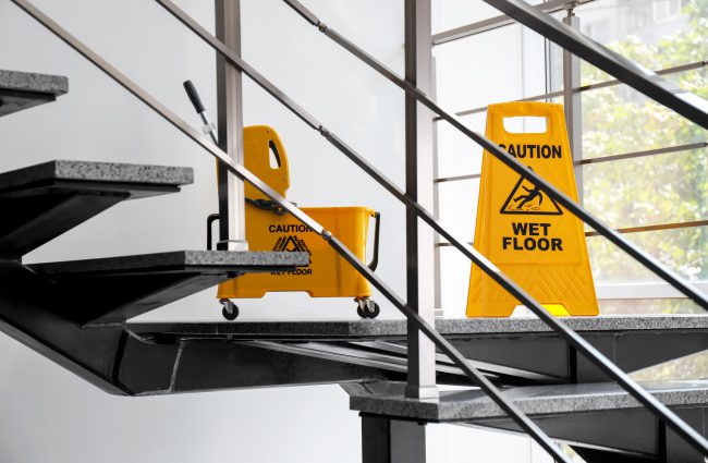 Safety sign with phrase Caution wet floor and mop bucket on stairs. Cleaning service